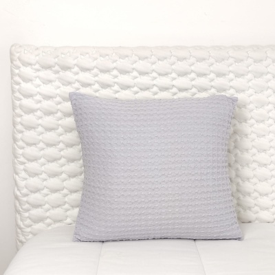 Almofada cinza quadrada com textura sobre cama branca com cabeceira acolchoada