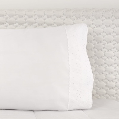 Almofada branca com bordas bordadas num fundo acolchoado branco com padrão texturizado