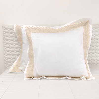 Almofadas brancas com bordadura em renda bege sobre cama branca