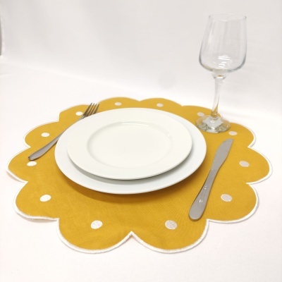 Conjunto de mesa com marcador amarelo com pontos brancos, pratos brancos, talheres metálicos e taça de vidro
