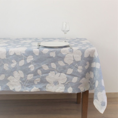 Toalha de mesa azul com flores brancas sobre mesa de madeira, com prato, garfo e taça
