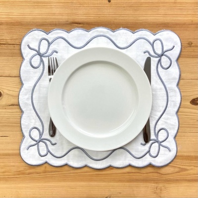 Conjunto de prato branco com talheres e toalhete bordado cinzento sobre mesa de madeira