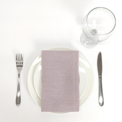 Conjunto de mesa com prato branco, guardanapo lilás, talheres prateados e copo de vidro