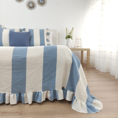 Cama com colcha às riscas azuis e brancas e almofadas decorativas, em quarto iluminado com decoração simples