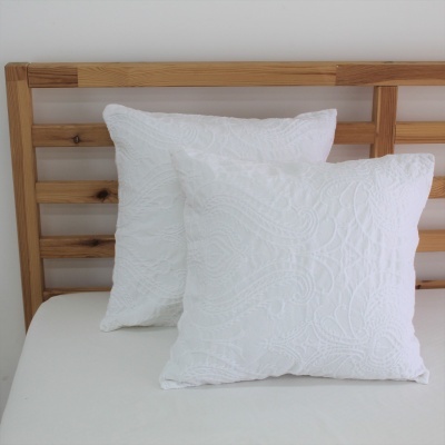 Duas almofadas brancas bordadas sobre cama com cabeceira de madeira