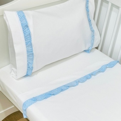 Lençol e fronha de bebé brancos com fita azul clara às bolinhas e folhos em berço branco