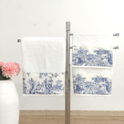 Conjunto de toalhas brancas com estampa azul penduradas em suporte metálico junto a vaso branco com flores rosas