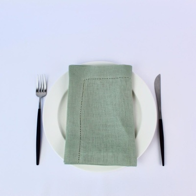 Guardanapo verde claro sobre prato branco com talheres pretos à esquerda e direita