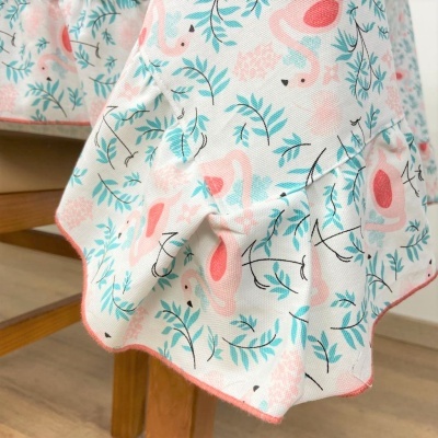 Pano branco com padrão de flamingos cor-de-rosa e folhas azuis pendurado numa mesa de madeira