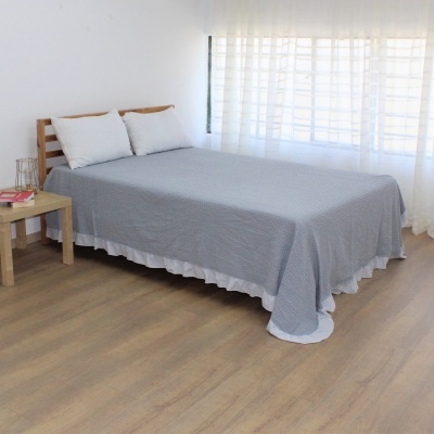 Cama com colcha cinzenta e almofadas brancas em quarto luminoso