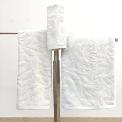 Toalhas brancas com padrão texturizado de folhas penduradas num suporte metálico numa casa de banho