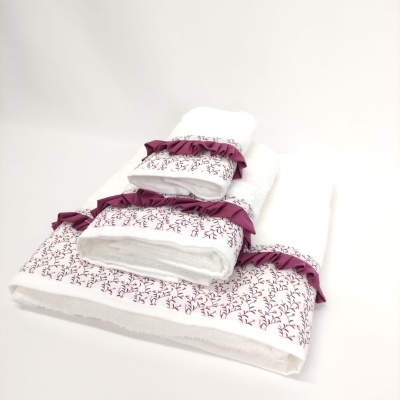 Conjunto de toalhas brancas com detalhes florais e folhos roxos.
