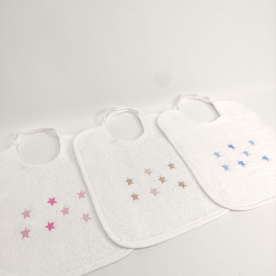 Três babetes brancos com estrelas coloridas em rosa, bege e azul