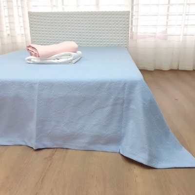 Cama com lençol azul e cobertores rosa e branco num quarto com piso madeira clara