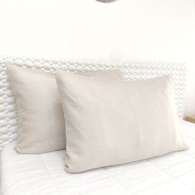 Duas almofadas beges numa cama com cabeceira branca texturada