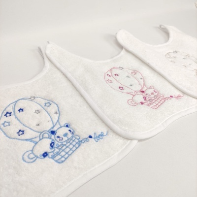 Três babetes brancos com bordados de ursinhos em balões de ar quente em azul, rosa e cinza