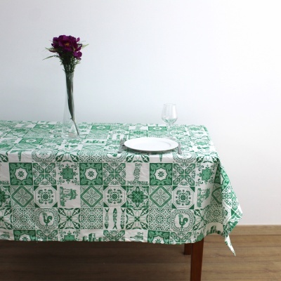 Toalha de mesa verde e branca com padrão geométrico em mesa de madeira com prato, copo e jarro com flores