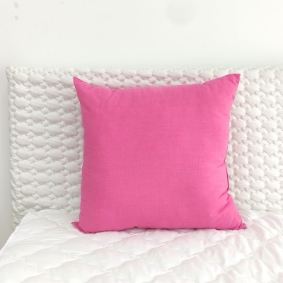 Almofada quadrada cor-de-rosa sobre cama branca texturizada