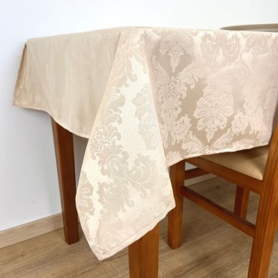 Toalha de mesa bege com padrão damasco sobre mesa de madeira clara