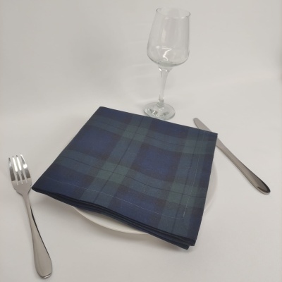 Mesa posta com prato branco, guardanapo xadrez azul e verde, garfo, faca e copo de vidro.