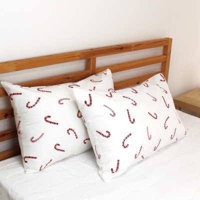 Duas almofadas brancas com desenhos de bengalas de Natal vermelhas sobre cama com cabeceira de madeira