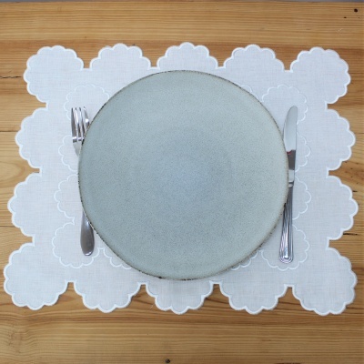 Prato cinzento com talheres em individual branco rendado sobre mesa de madeira