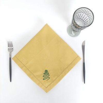 Guardanapo amarelo com árvore de Natal bordada, garfo, faca e copo de vidro