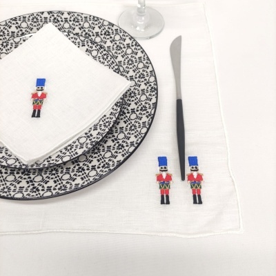 Conjunto de mesa com pratos brancos e padrão preto, guardanapo e toalha branca com bordados de soldadinhos coloridos
