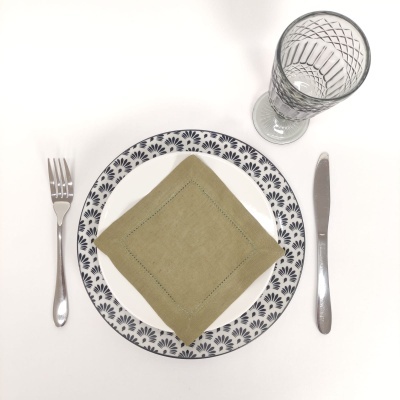 Conjunto de jantar com prato azul e branco, guardanapo verde, talheres metálicos e copo de vidro gravado.