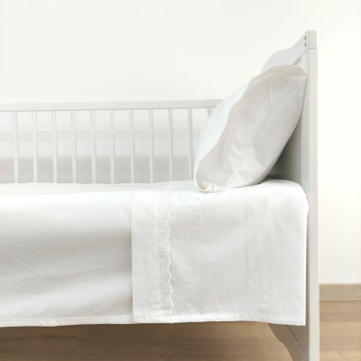 Cama branca de madeira com lençol e fronha brancos bordados