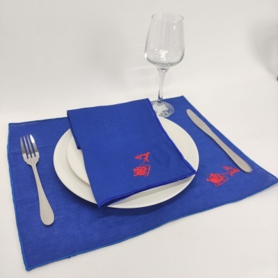 Jogo americano azul com guardanapo azul e bordado vermelho, prato branco e talheres prateados