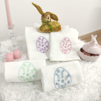 Toalhas brancas com bordados de ovos coloridos e decoração de Páscoa com coelho e velas