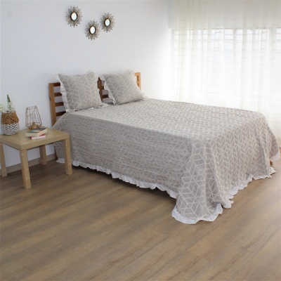 Colcha bege com padrão geométrico e almofadas no quarto com piso de madeira clara