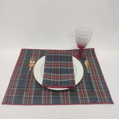 Jogo americano xadrez com prato branco, talheres dourados, copo vermelho e guardanapo