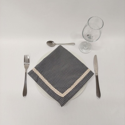 Posto de mesa com prato branco, guardanapo xadrez azul escuro e branco, talheres prateados e copo de vidro.