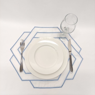 Mesa posta com pratos brancos, talheres metálicos, copo de vidro e individual branco com bordas azuis.