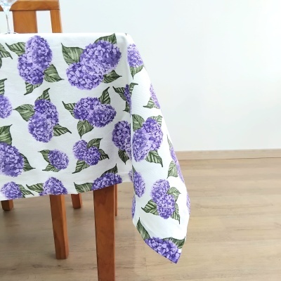 Mesa com toalha branca com flores roxas e folhas verdes