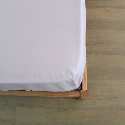 Canto de cama com estrutura de madeira e lençol branco.