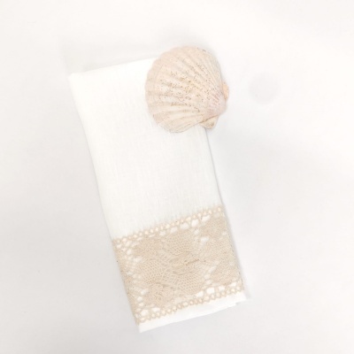 Toalha branca com faixa rendada bege e concha do mar sobre superfície branca