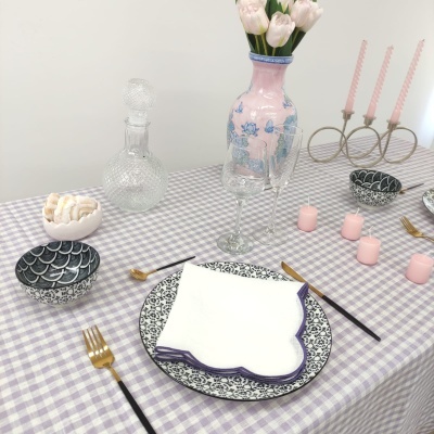 Mesa posta com pratos, talheres, velas e decoração em tons lilás, branco e dourado