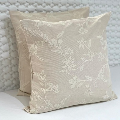 Duas almofadas quadradas bege com padrão floral bordado em fundo branco texturizado
