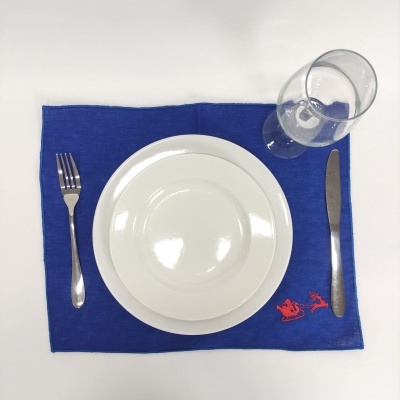 Conjunto de jantar com prato, garfo, faca e copo sobre individual azul com bordado vermelho