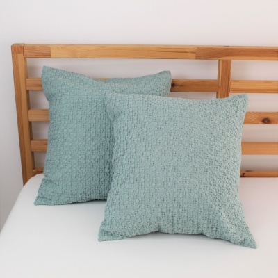 Duas almofadas verdes claras com textura sobre cama branca e cabeceira de madeira clara