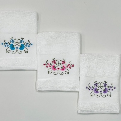 Três toalhas brancas com bordados florais em azul, rosa e lilás