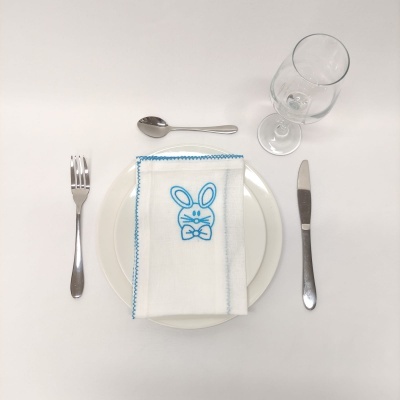 Mesa posta com prato, talheres, copo e guardanapo bordado com coelho azul