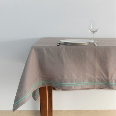 toalha de mesa cinzenta com linha verde sobre mesa de madeira com prato e taça