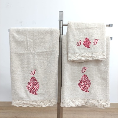 Conjunto de toalhas creme com bordados vermelhos e renda exibidas em suporte metálico