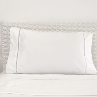 Almofada branca com fronhas rendilhadas sobre colchão branco texturado