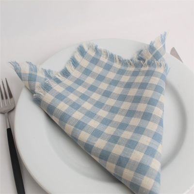 Guardanapo quadrado azul claro e branco dobrado em triângulo em prato branco com garfo ao lado