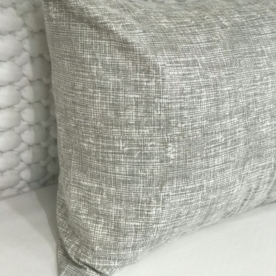 Almofada cinza com padrão de linhas sobre superfície branca e parede acolchoada branca